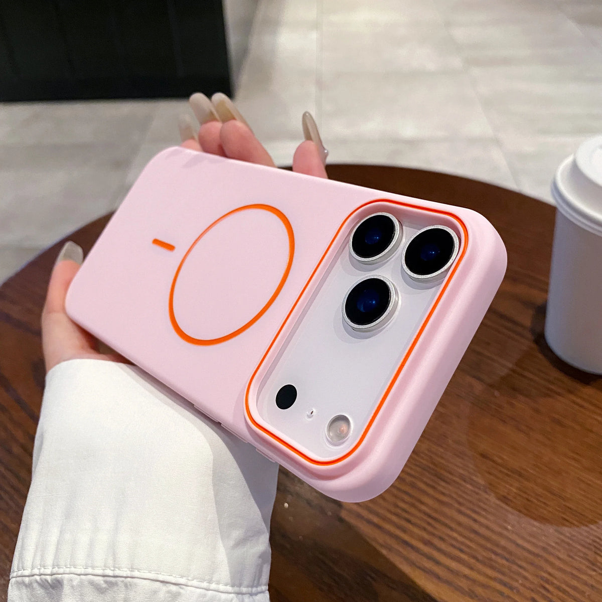A pink magnetic wireless charging phone case is held by a hand on a wooden surface.