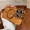 A hand holds a gold-plated magnetic clear case for an iPhone on a wooden surface.