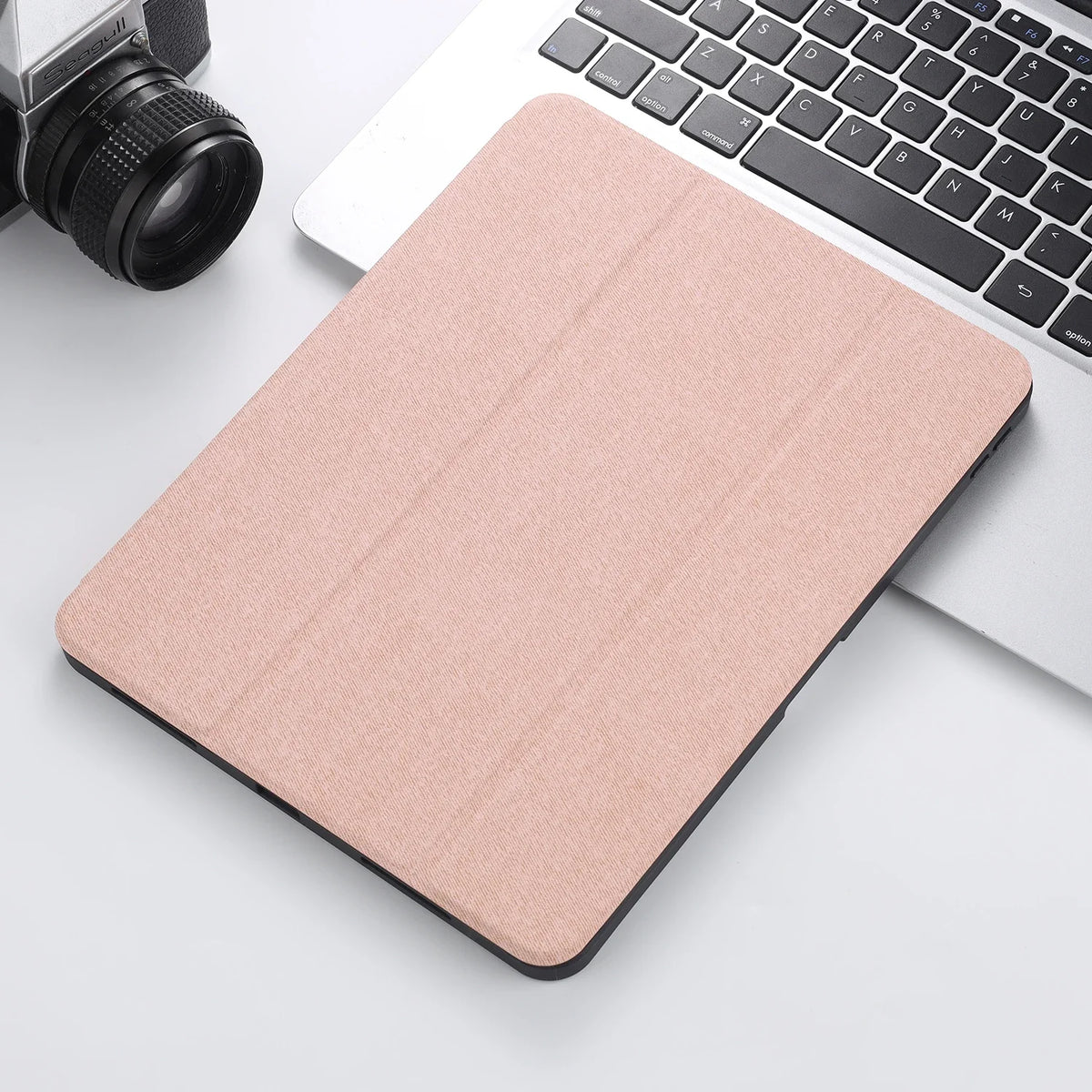 A pink retro marbling skin for an iPad Pro placed next to a silver laptop and a camera.