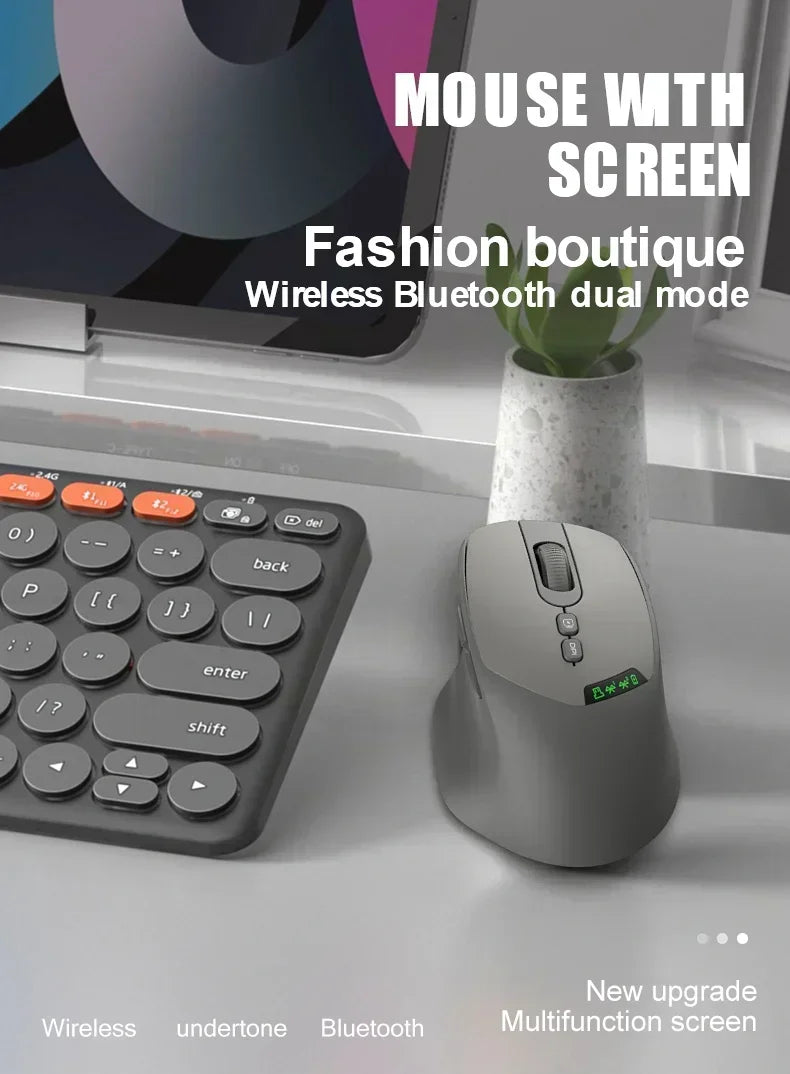 A gray wireless mouse with a multifunction screen is shown next to a laptop and a potted plant.