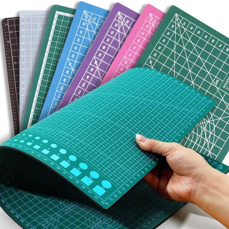 A hand holds a double-sided self-healing cutting mat with grid guides showing various colors and patterns.