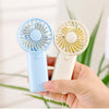 A hand holds two portable rechargeable mini handheld fans, one blue and one white.