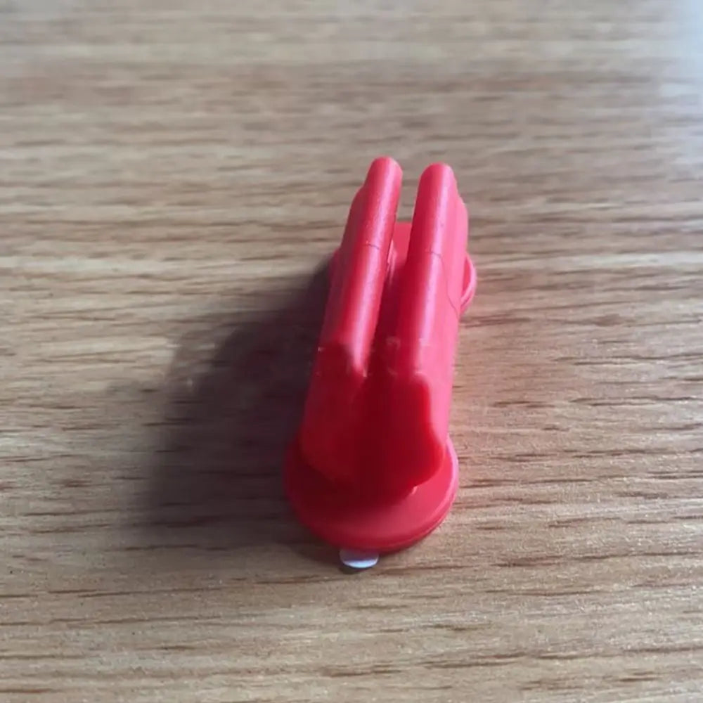 A red silicone self-adhesive pen holder with two prongs resting on a wooden surface.