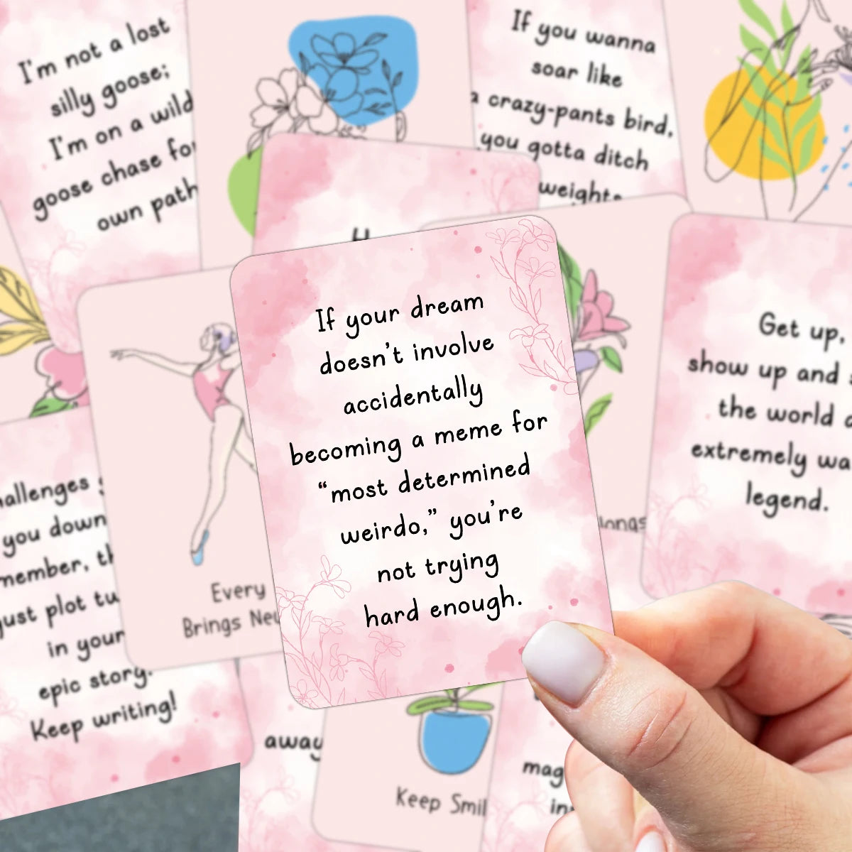 A hand holds a stack of pink affirmation cards with positive messages written on them.