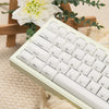 A close-up view of a white mechanical keyboard with custom printed jelly keycaps resting on a beige knitted surface.