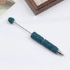 A silver pen accessory with a teal blue rhinestone bead on the tip and a textured body.
