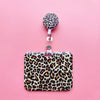 A leopard print ID holder with a matching lanyard and keychain displayed on a pink background.