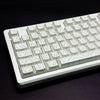 Vista cercana de un teclado mecánico blanco con teclas degradadas de contorno sobre una superficie oscura.