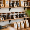 Row of glass jars filled with coffee beans and brown paper bags labeled for coffee products