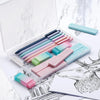 An open clear pencil case filled with a set of pastel colored mechanical pencils resting on a white marble surface.