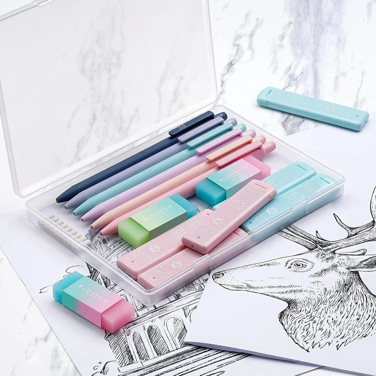 An open clear pencil case filled with a set of pastel colored mechanical pencils resting on a white marble surface.