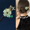 Accessoire de cheveux floral en bois avec une fleur vert pâle, des accents dorés et des perles vertes.