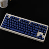 A close-up view of a white mechanical keyboard with dark blue PBT keycaps and cherry profile switches.