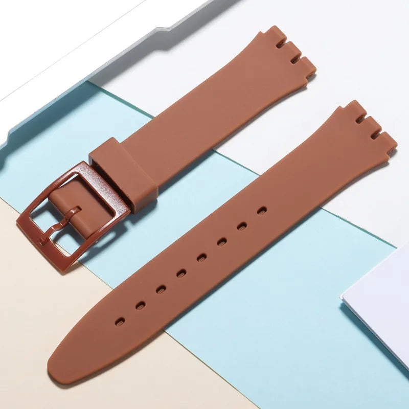 A brown silicone watch strap is shown with replacement tools, laid out on a light background.
