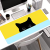 A yellow and light blue cat design mouse pad is placed on a white desk next to a computer.
