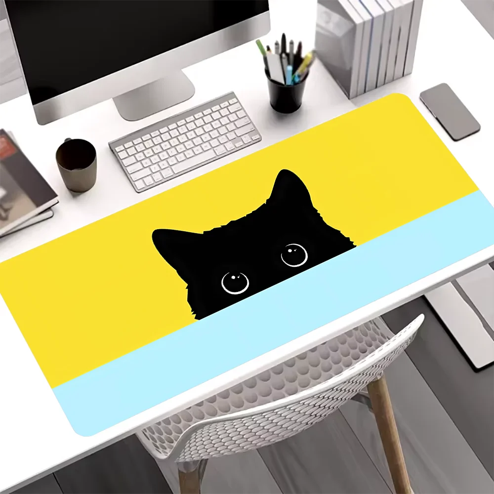 A yellow and light blue cat design mouse pad is placed on a white desk next to a computer.