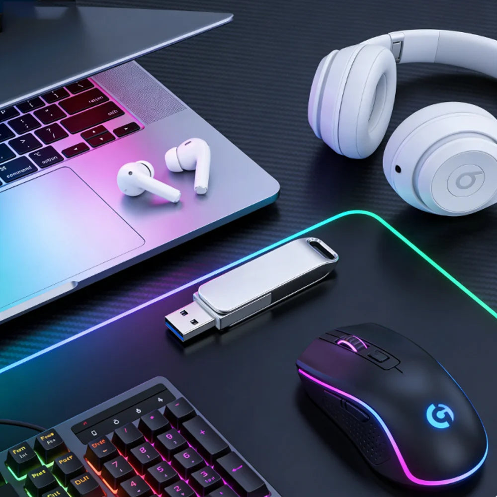 A collection of electronic devices including a laptop, headphones, a flash drive, and a gaming mouse on a dark surface.
