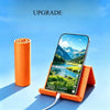 An orange flexible silicone phone stand holding a smartphone displaying a scenic mountain landscape.