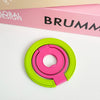 A bright pink and lime green magnetic phone grip and stand with a foldable ring resting on a white surface.