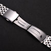 A close-up of a stainless steel watch band with a folding safety clasp shown against a dark background.