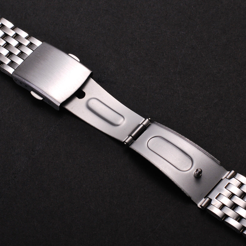 A close-up of a stainless steel watch band with a folding safety clasp shown against a dark background.