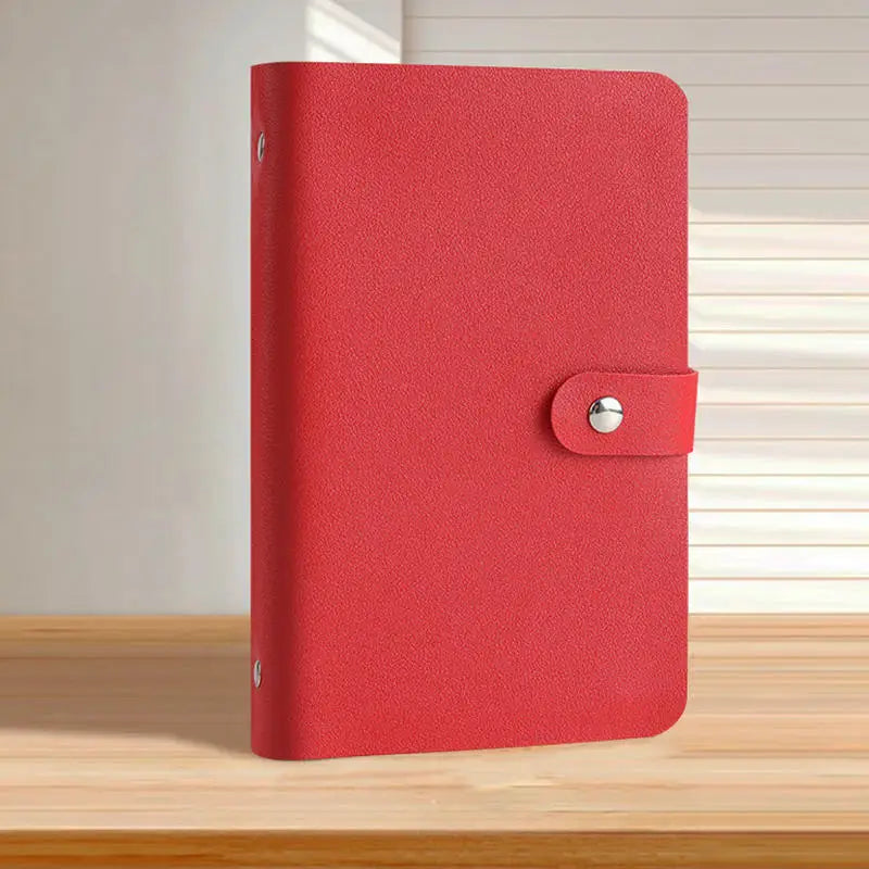 A red binder with a pink leather cover and silver clasp resting on a wooden surface.