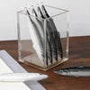 A clear acrylic container holds several silver and black ocean fish ballpoint pens on a wooden surface.