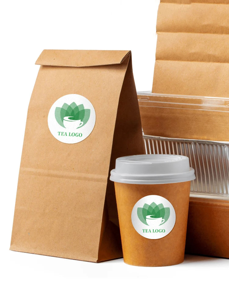 A brown paper bag and a disposable cup both feature a green tea logo sticker.