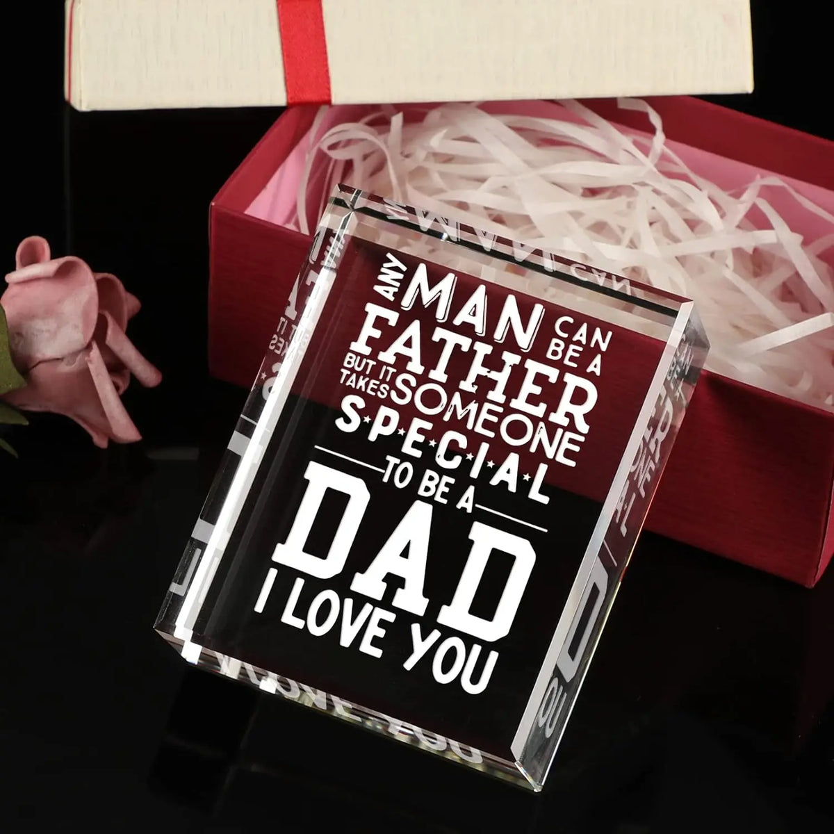A clear glass keepsake box filled with white paper shreds, resting on a dark surface.