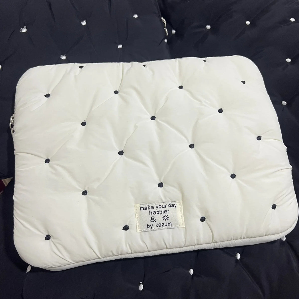 A white quilted padded laptop sleeve case with small black dots on a dark fabric background.