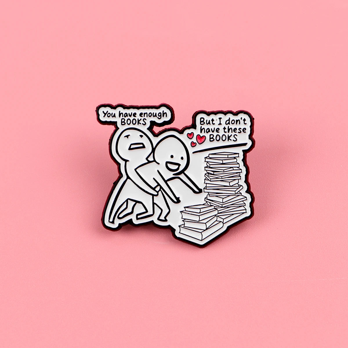 A black enamel lapel pin featuring two figures and text about having enough books versus not having them.
