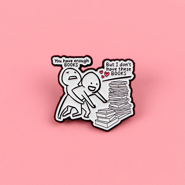A black enamel lapel pin featuring two figures and text about having enough books versus not having them.