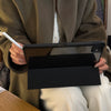 Eine Person hält eine schwarze Lederhülle für ein Apple iPad vor einem braunen Mantel.