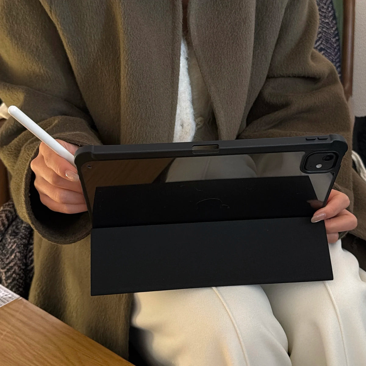 Eine Person hält eine schwarze Lederhülle für ein Apple iPad vor einem braunen Mantel.