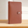 A brown leather-look binder with a stitched cover and a silver clasp resting on a wooden surface.