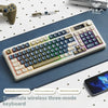 A white wireless three-mode keyboard with blue and purple keys is shown on a dark surface next to a smartphone.