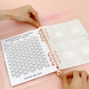 A hand is using a pink envelope budget binder set to track savings with numbered envelopes.