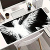 A black and white artistic angel wing desk mat mouse pad displayed on a white desk.
