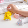 A yellow tiger-shaped silicone wrist rest and a pink pig-shaped silicone wrist rest are shown next to a hand typing on a whit