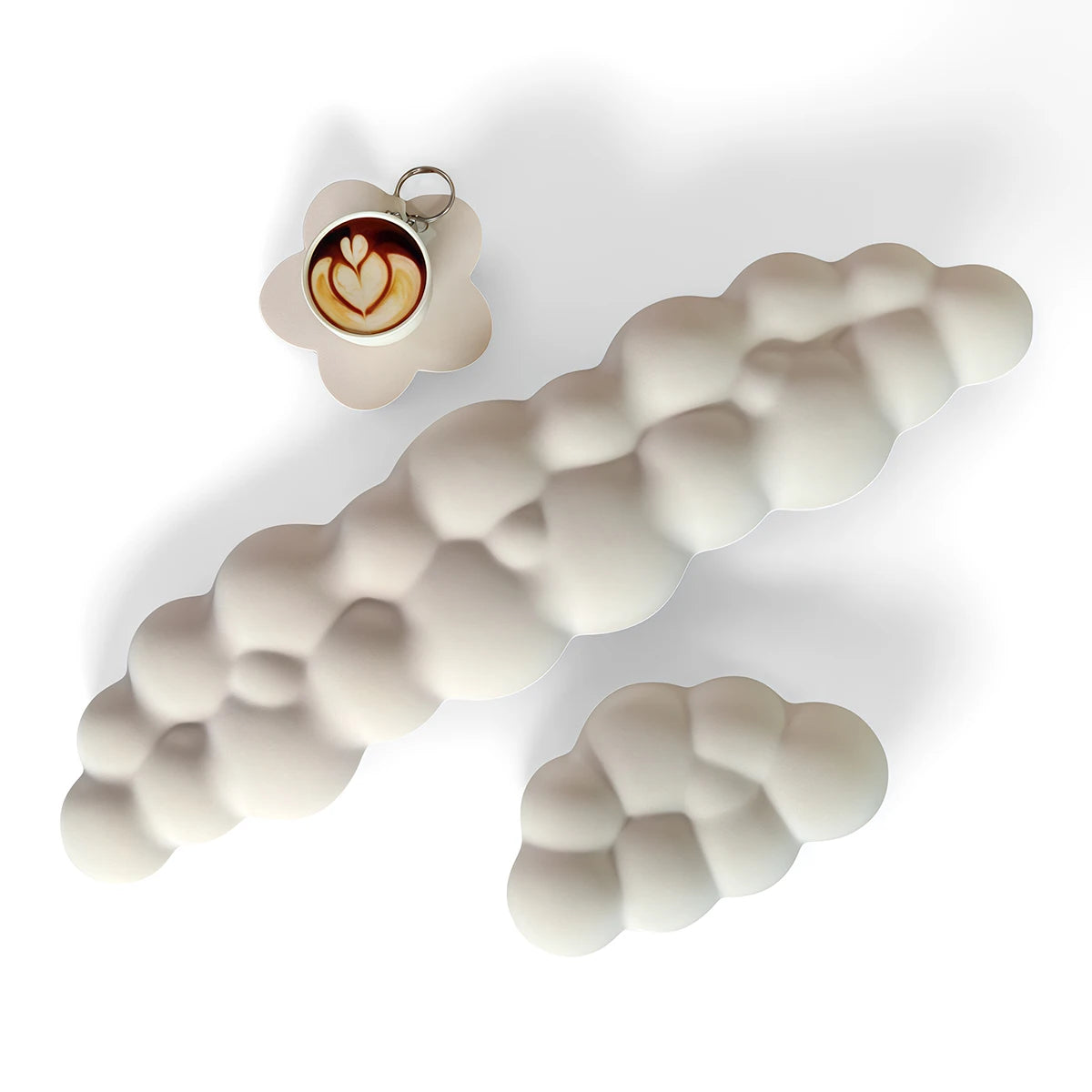 Un set de trois repose-poignets pour clavier en forme de nuage blanc, dont un avec une décoration latte art.
