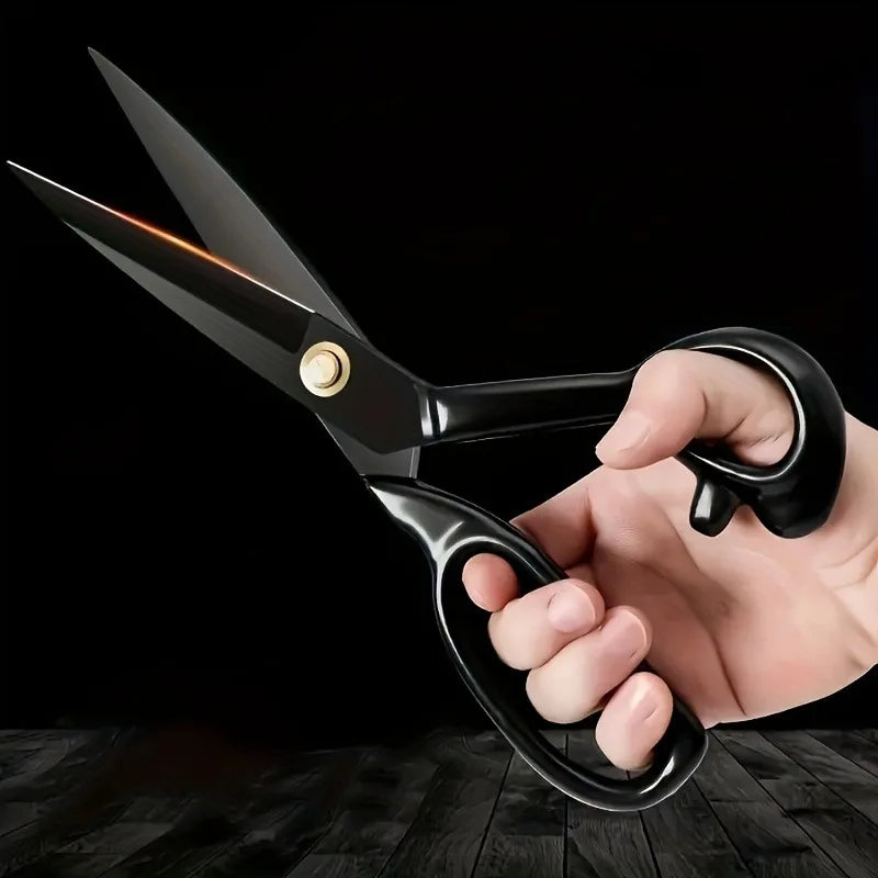 A hand is holding a pair of black tailor scissors with sharp blades visible against a dark background.