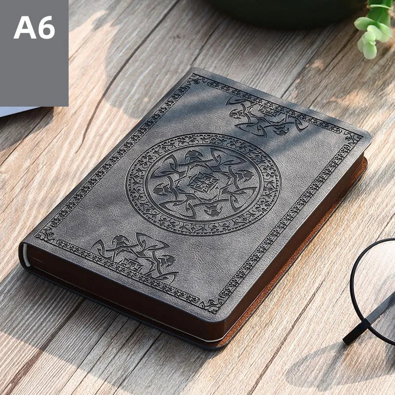 A dark gray retro PU leather pocket notebook with an embossed circular design resting on a wooden surface.