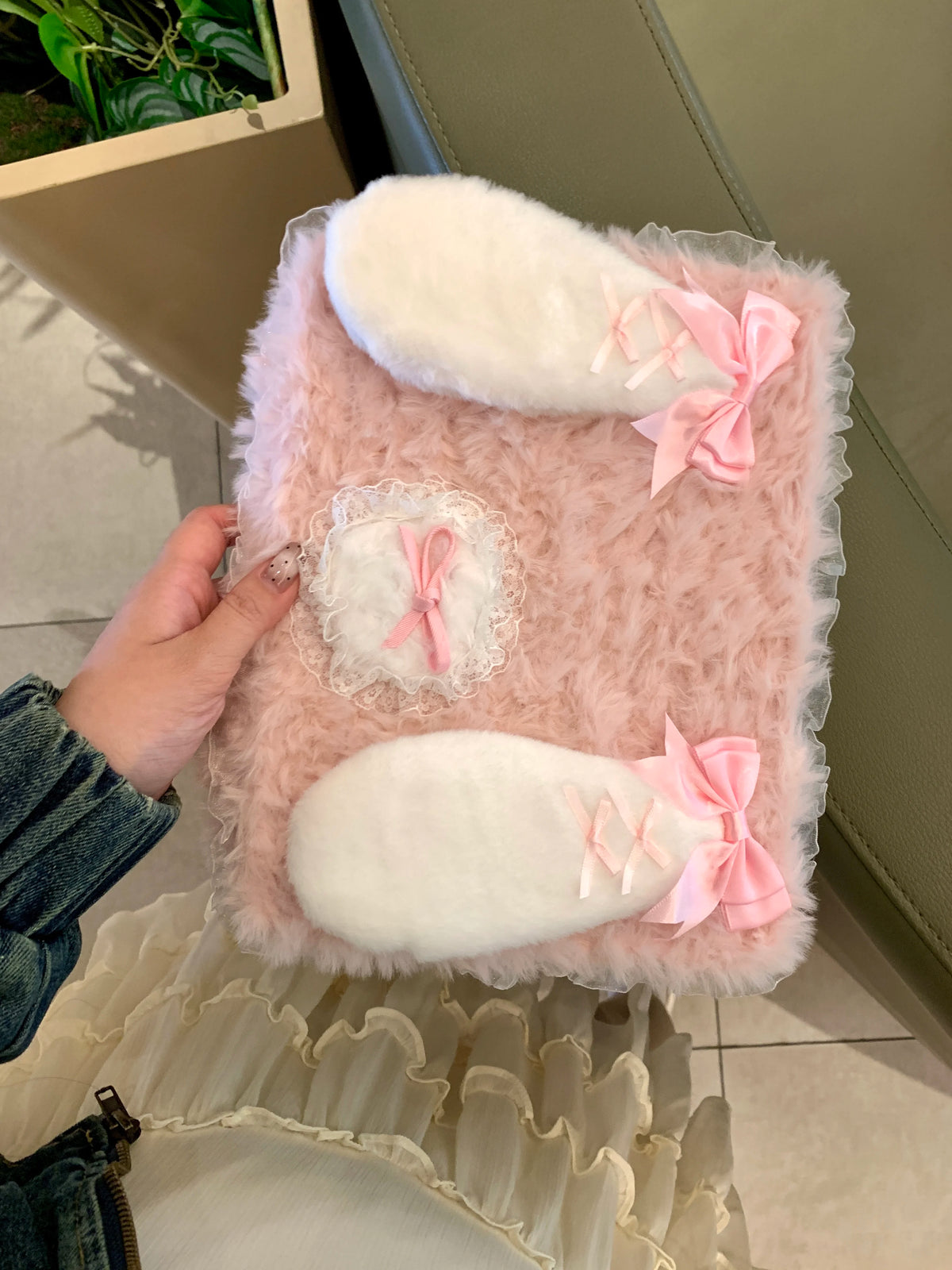 A pink fluffy rabbit plush case with white accents is shown resting on a light-colored surface.