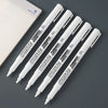 Three white permanent paint markers are displayed diagonally against a gray background.