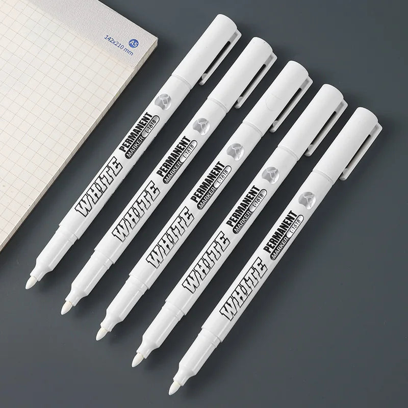 Three white permanent paint markers are displayed diagonally against a gray background.
