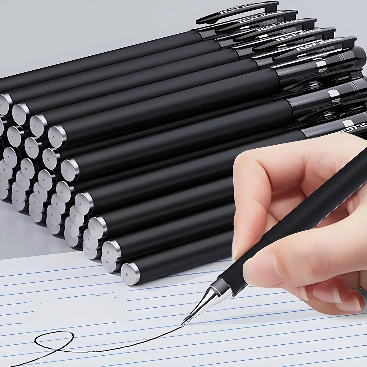A hand holds a set of black precision gel pens with fine tips writing on lined paper.