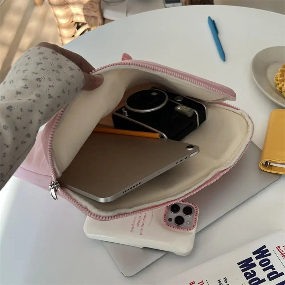 A beige laptop sleeve case is open, showing a silver tablet and a black camera inside on a white table.