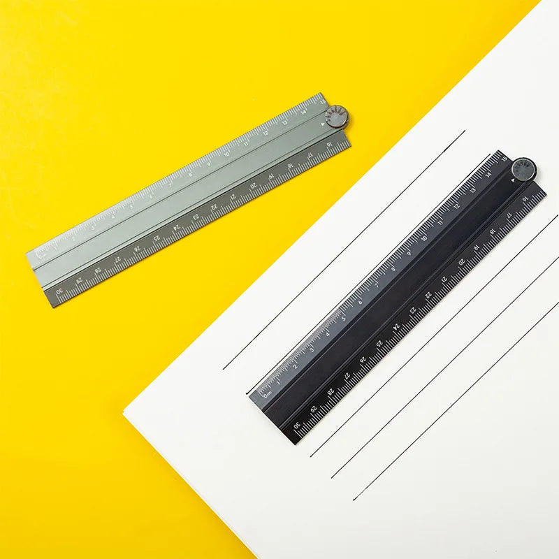 A precision aluminum folding ruler is shown lying on a yellow surface next to a white sheet of paper.