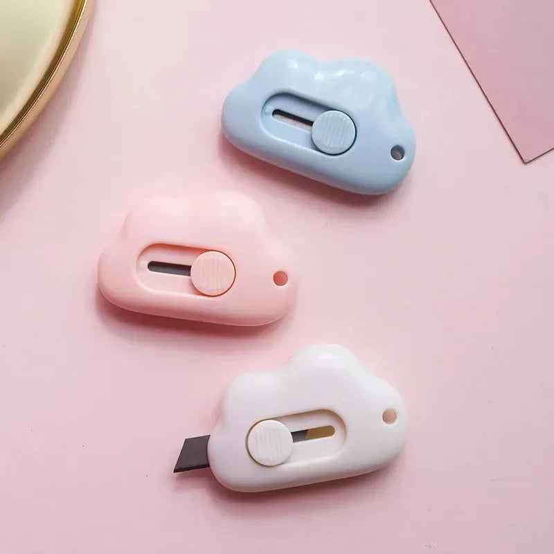 A set of three multi-color rabbit cloud utility knives in light blue, pink, and white resting on a pink surface.