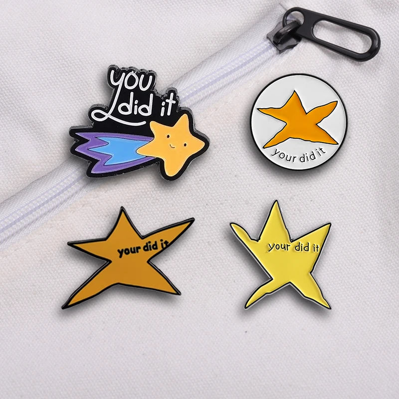 A set of three enamel pins featuring a star design with the text you did it on a white fabric background.